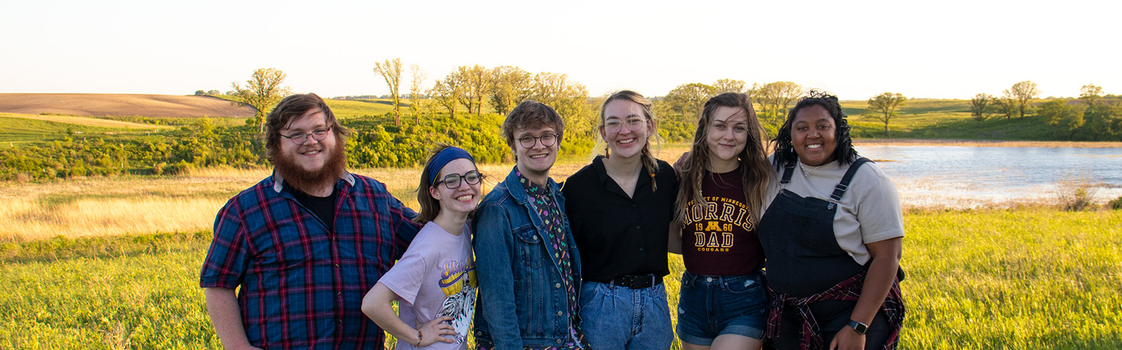 A group of students in front of a prairie landscape smiles into lens